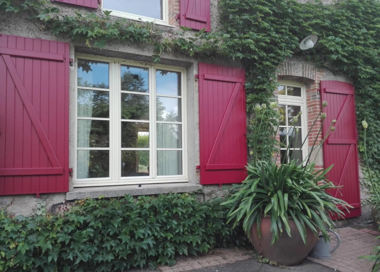 façade de maison tout en verdure avec des volets battants rouges